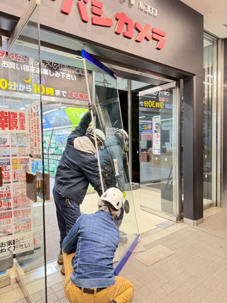 大型テナントビルさんの割れたがらすのところにあたらしいガラスドアをはめ込む写真
