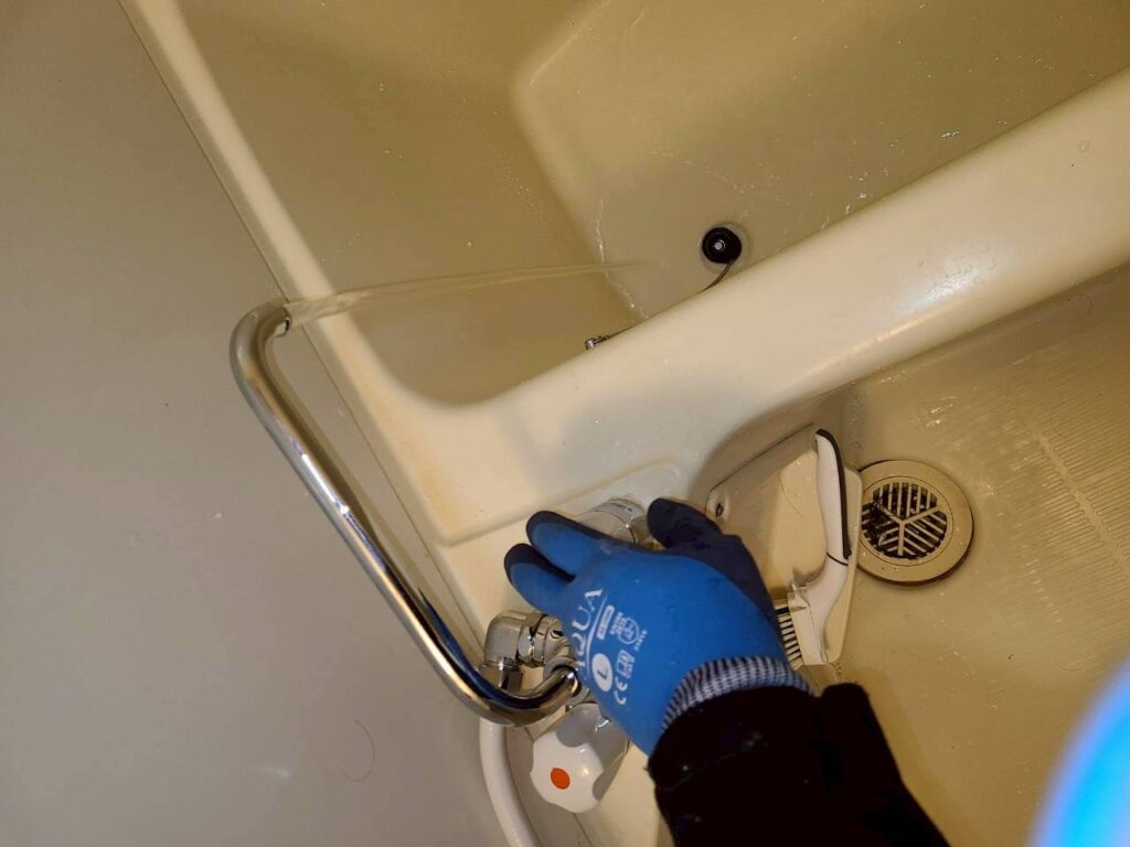 品川区小山の賃貸マンション浴室で作業員が新しい物と交換して確認している写真