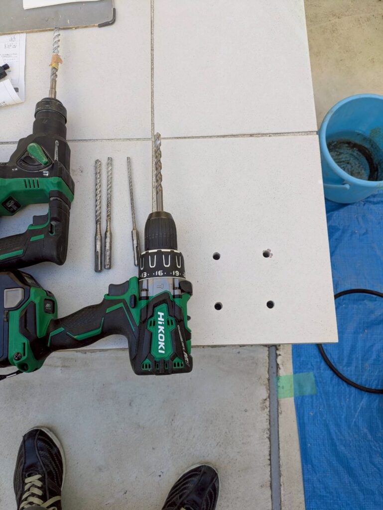 目黒区目黒本町のアパートの踊り場手すり位置テープを剥がしてまたハンマードリルで穴を開けている写真