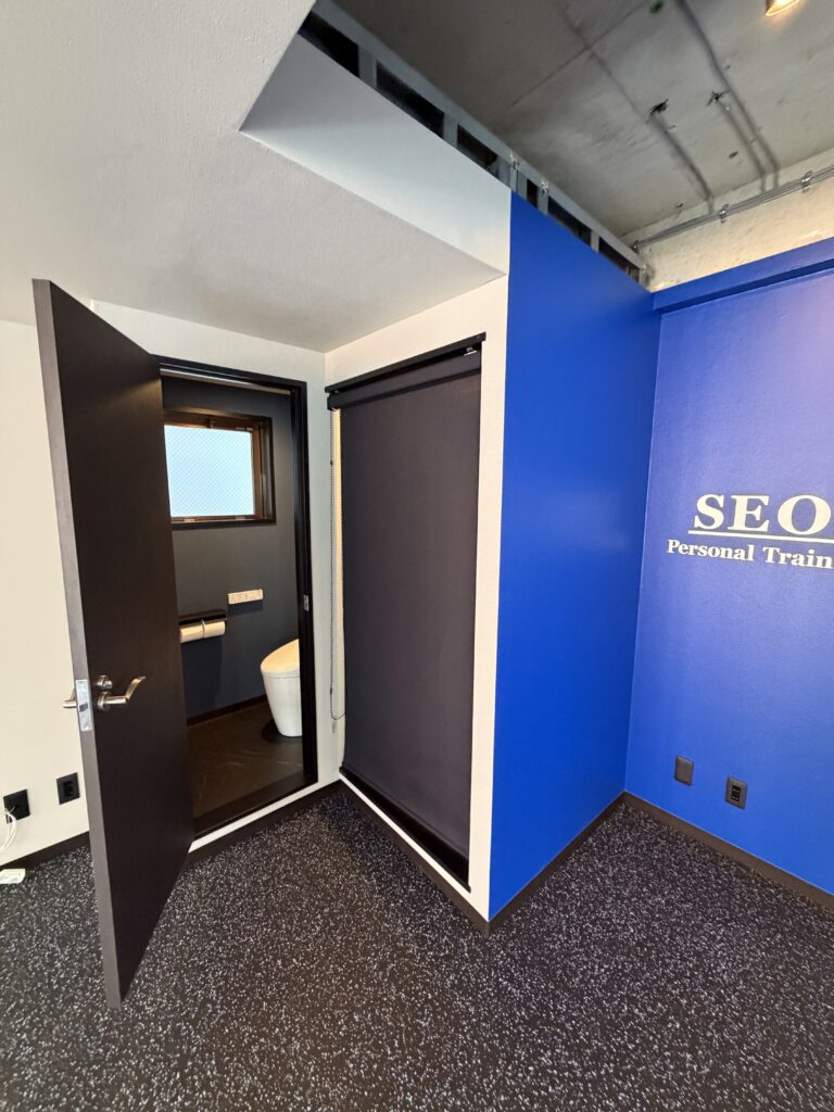 品川区五反田のジムの開いたトイレドア青いサイン壁、ラバー床の写真